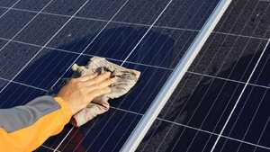 A close up of an arm and a hand holding a cloth, cleaning dust off of a solar panel
