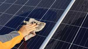 A close up of an arm and a hand holding a cloth, cleaning dust off of a solar panel A close up of an arm and a hand holding a cloth, cleaning dust off of a solar panel